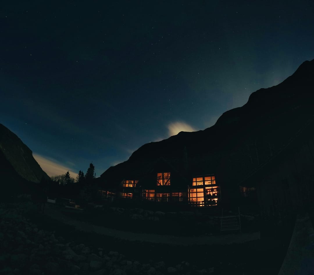 Chalet mit beleuchteten Fenstern am Fuss eines Berges bei Nacht